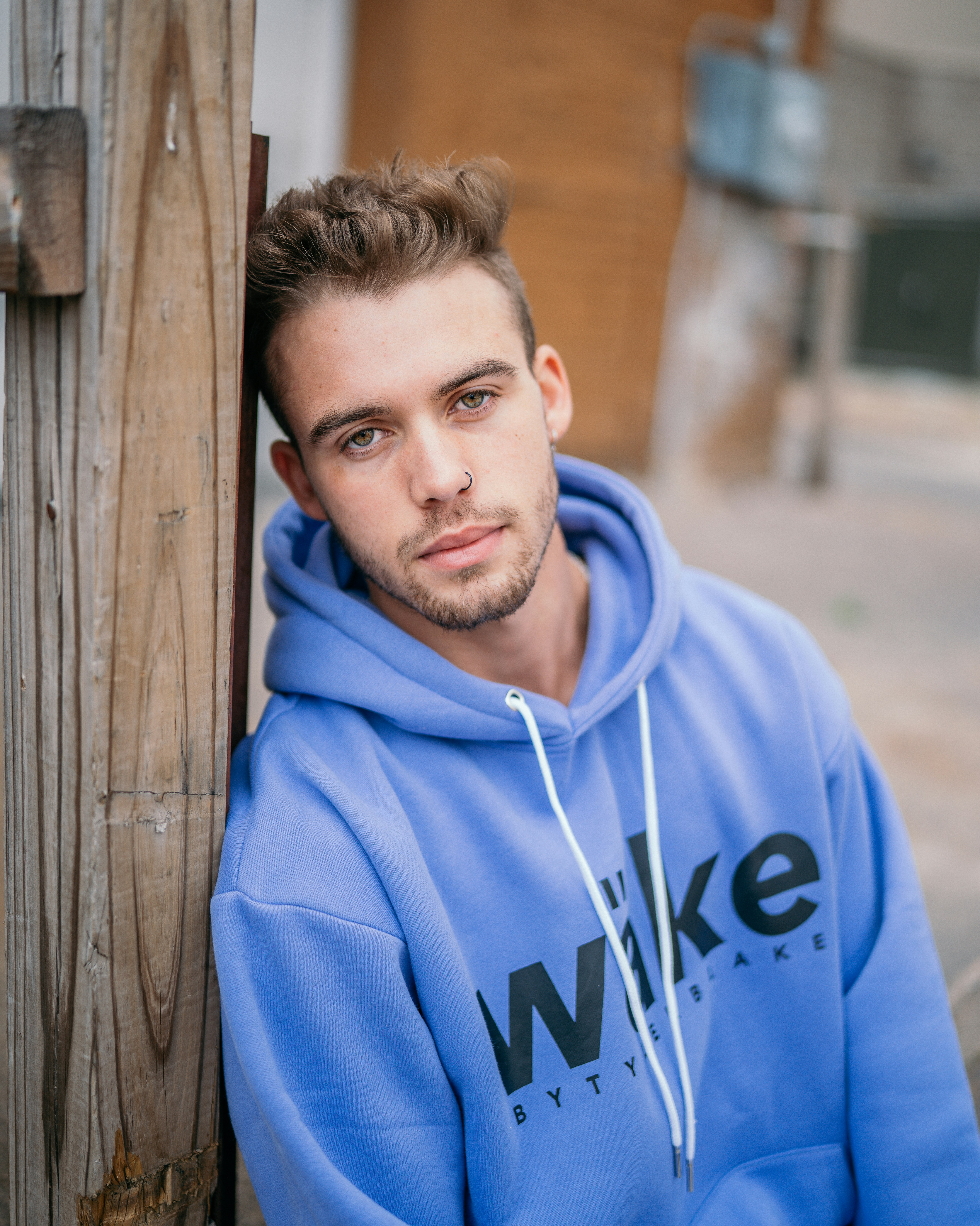 man in blue hoodie standing beside brown wooden fence